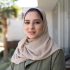 istockphoto-1393101439-612×612 Head and shoulders view of woman in khaki green abaya and beige hijab standing outside family home and smiling at camera.